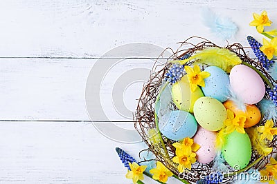 Ð¡olorful Easter eggs in nest, feather and spring flowers on white table top view. Holiday card or banner Stock Photo